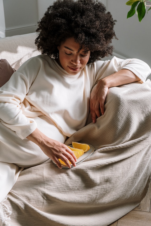 Een zwangere vrouw die op bed ligt op bed met een bordje gesneden Sinasappels.