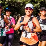 Vrouwelijke hardlopers met startnummers en hydratatievesten tijdens een zomerse trailrun, ideaal voor hardlopen voor beginners