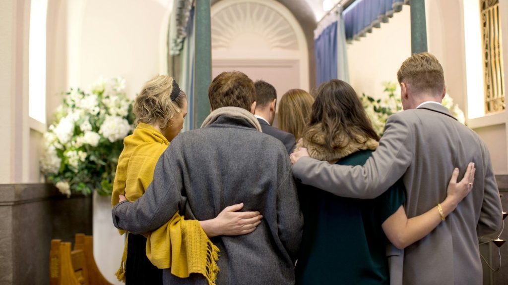 Mensen troosten elkaar tijdens een afscheidsdienst