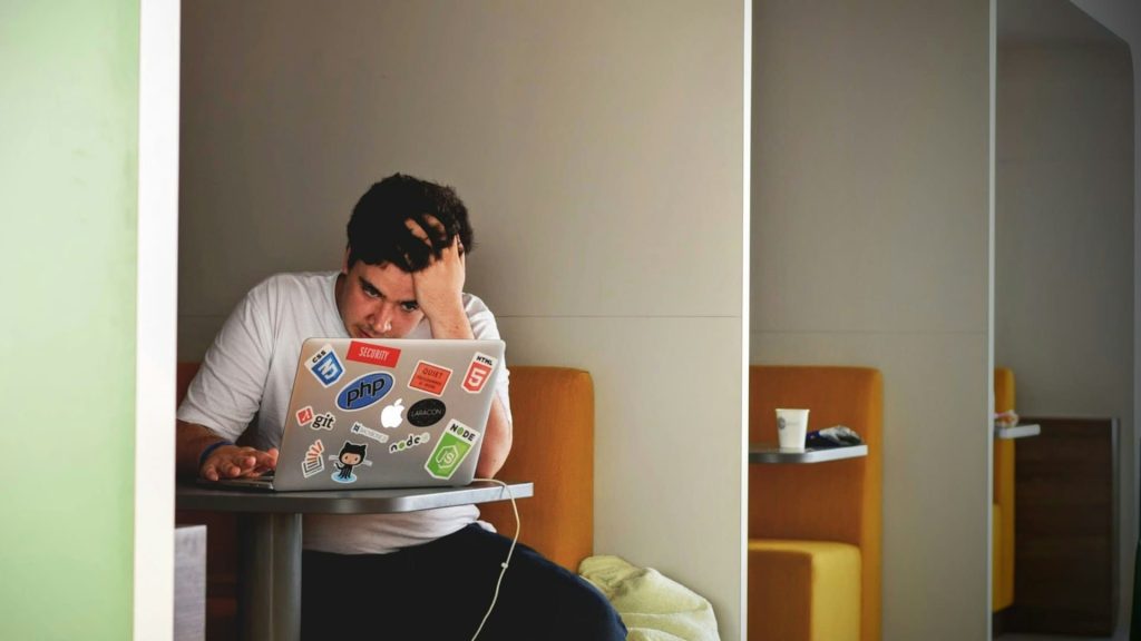 Man kijkt gefrustreerd naar laptop tijdens stressvolle beslissing onder druk