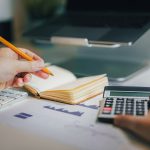 Persoon controleert cijfers met rekenmachine en laptop om btw-aangifte fouten te voorkomen